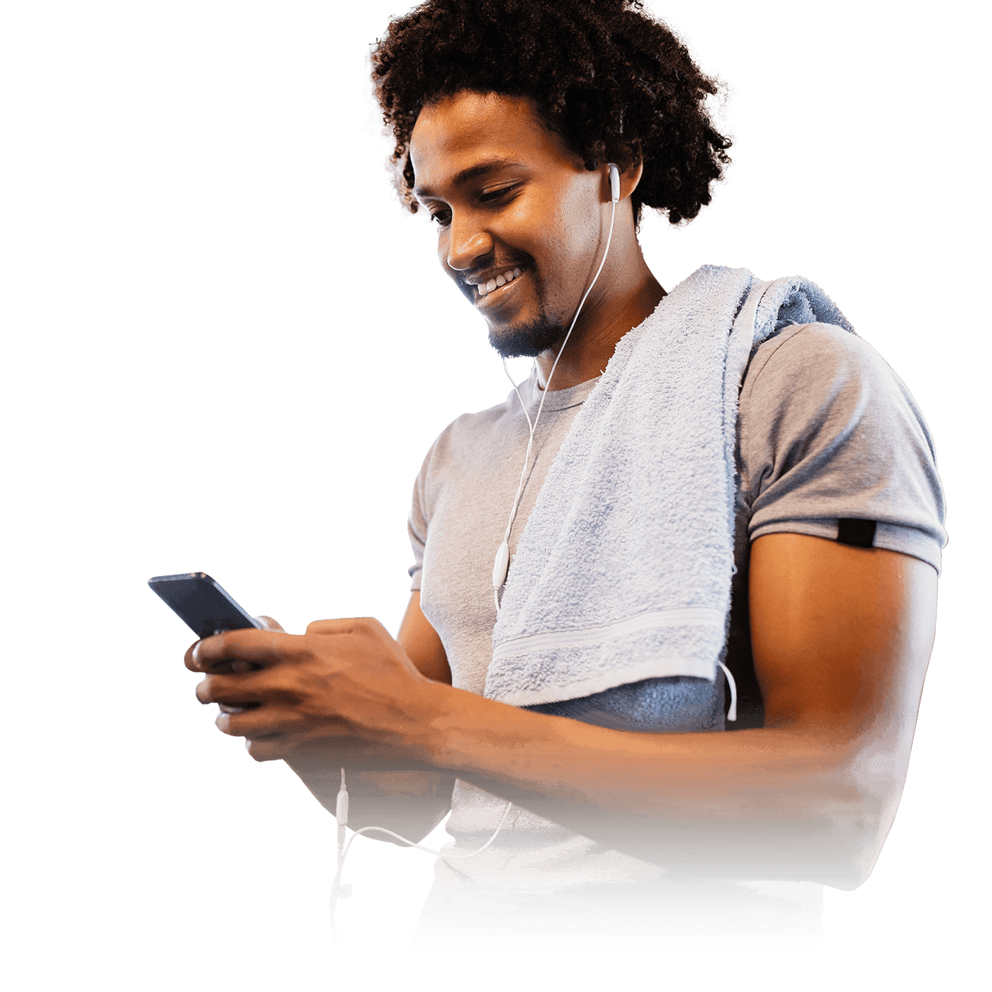 A man in a gray t-shirt with a towel over his shoulder, holding a phone with earphones plugged in.