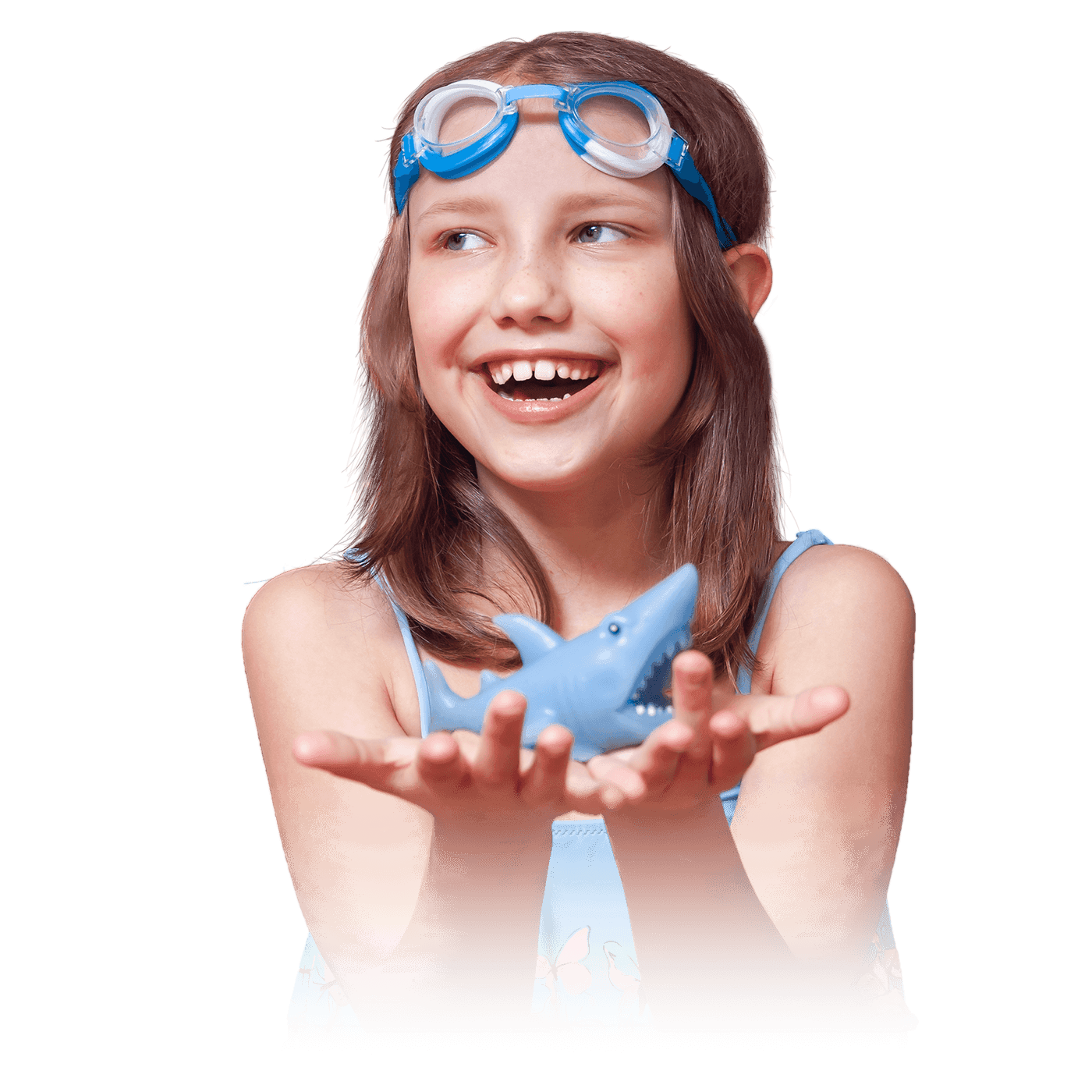 A young girl smiling with swim goggles on her forehead, holding a toy shark in her hand.